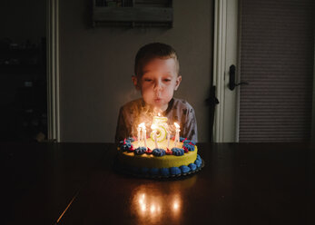 Boy blowing birthday candles on table at home - CAVF59502