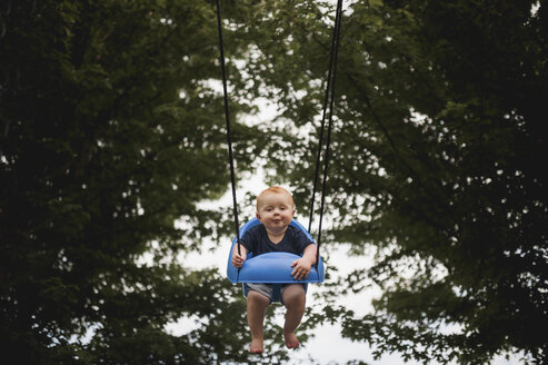 Porträt eines niedlichen kleinen Jungen, der auf dem Spielplatz gegen Bäume schaukelt - CAVF59511