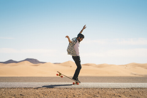 Mann skateboarding auf der Straße gegen blauen Himmel während sonnigen Tag, lizenzfreies Stockfoto