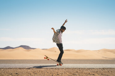 Man skateboarding on road against blue sky during sunny day - CAVF59574