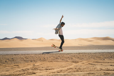 Side view of man skateboarding on road against blue sky during sunny day - CAVF59575