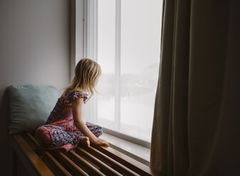 Seitenansicht eines Mädchens, das durch das Fenster schaut, während es zu Hause sitzt - CAVF59592