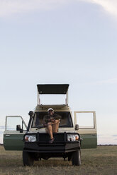 Mann in voller Länge auf Fahrzeug sitzend im Serengeti-Nationalpark gegen den Himmel - CAVF59603