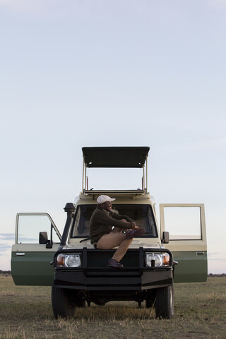 Seitenansicht eines auf einem Fahrzeug sitzenden Mannes im Serengeti-Nationalpark gegen den Himmel, lizenzfreies Stockfoto