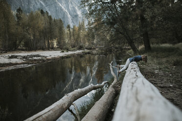 Seitenansicht eines Jungen, der auf einem Baumstamm am See im Yosemite National Park liegt - CAVF59621