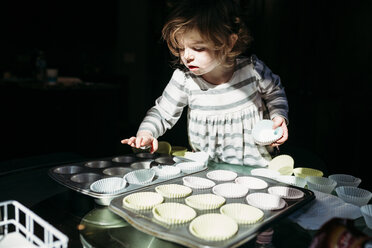 Niedliches Mädchen arrangiert Cupcake-Halter im Backblech - CAVF59629