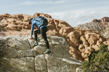 Weiblicher Wanderer mit Rucksack klettert an einem sonnigen Tag auf Felsen - CAVF59639