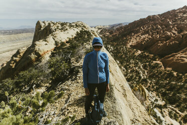 Female hiker with backpack wearing jacket and cap while standing on mountain during sunny day - CAVF59641