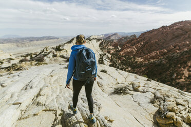 Rückansicht einer Wanderin mit Rucksack, die an einem sonnigen Tag auf einem Felsen läuft - CAVF59642