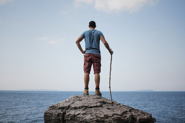 Rückansicht eines Wanderers, der mit der Hand an der Hüfte einen Stock hält, während er auf einem Felsen vor dem Meer und dem Himmel im Bruce Peninsula National Park steht - CAVF59652
