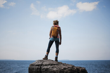 Rückansicht einer Wanderin mit Rucksack auf einem Felsen vor dem Meer und dem Himmel im Bruce Peninsula National Park - CAVF59653