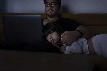 Vater benutzt nachts seinen Laptop auf der Couch, während seine Tochter zuschaut - ERRF00301