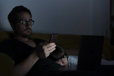 Vater benutzt Laptop und Mobiltelefon nachts auf der Couch, während seine Tochter schläft - ERRF00304