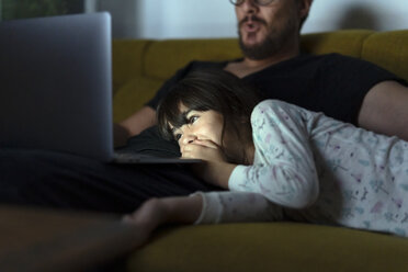 Glückliche Tochter und Vater schauen nachts auf der Couch auf den Laptop - ERRF00309