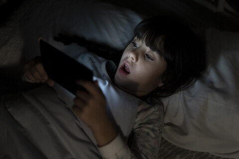 Schockiertes Mädchen liegt im Bett und benutzt nachts ihr Smartphone, lizenzfreies Stockfoto
