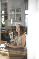 Mature woman sitting in coffee shop with smartphone and digital tablet - MOEF01886