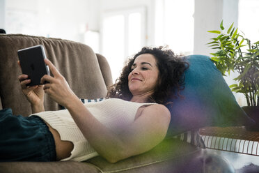 Reife Frau auf Couch liegend, mit digitalem Tablet - MOEF01903