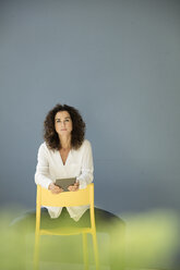 Businesswoman sitting on yellow chair, holding digital tablet - MOEF01908