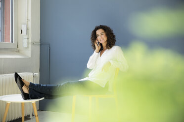 Businesswoman talking on the phone, sitting in office with feet up - MOEF01909