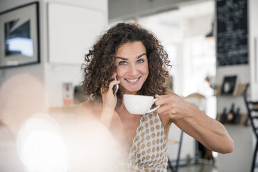 Reife Frau sitzt im Café, telefoniert, trinkt Kaffee - MOEF01926