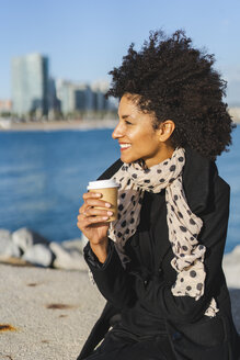 Spanien, Barcelona, lächelnde Frau auf einer Mauer sitzend mit Kaffee zum Mitnehmen - AFVF02070