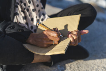 Frau sitzt an einer Wand und schreibt in ein Notizbuch, Nahaufnahme - AFVF02075