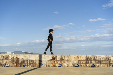 Spanien, Barcelona, schwarz gekleidete Frau, die bei Sonnenlicht auf einer Mauer läuft - AFVF02080