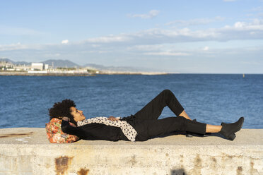 Spanien, Barcelona, schwarz gekleidete Frau, die sich auf einer Mauer vor dem Meer ausruht - AFVF02084