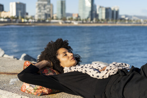 Spanien, Barcelona, schwarz gekleidete Frau, die sich bei Sonnenlicht an einer Mauer ausruht, lizenzfreies Stockfoto