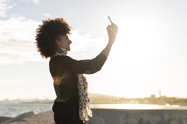 Lächelnde Frau nimmt Selfie mit Smartphone in der Nähe des Meeres - AFVF02096