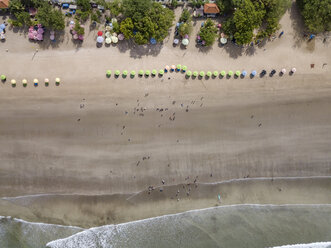 Bali, Kuta Beach, Reihe von Sonnenschirmen und Menschen am Strand, Luftaufnahme - KNTF02508