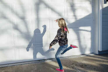 Full length of girl dancing on footpath against wall - CAVF59685