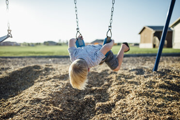 Boy playing on swing at park during sunny day - CAVF59692