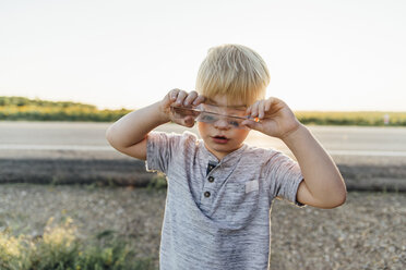 Boy playing with glass toy while standing on field - CAVF59695