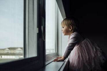 Side view of girl standing by window at home - CAVF59708