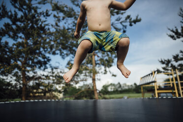 Low section of shirtless boy jumping on trampoline at park - CAVF59719