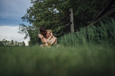 Mutter umarmt fröhlichen Sohn auf einer Wiese im Park - CAVF59720