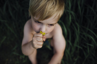 High angle view of shirtless boy smelling flower at park - CAVF59721