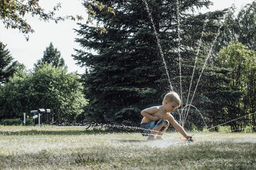 Side view of shirtless boy playing with sprinkler at park - CAVF59723