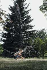 Hemdloser Junge spielt mit Sprinkleranlage im Park - CAVF59724