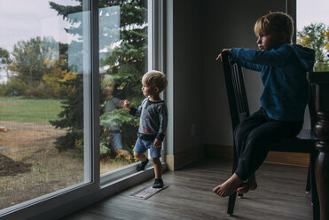 Nachdenkliche Brüder schauen durch das Fenster zu Hause - CAVF59727