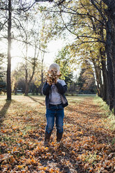 Verspielter Junge hält Herbstblätter im Park an sein Gesicht - CAVF59739