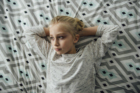 Overhead view of thoughtful girl with hands behind head lying on bed stock photo