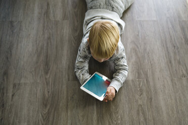 High angle view of boy using tablet computer while lying on floor at home - CAVF59753