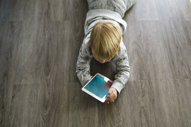Hochformatige Ansicht eines Jungen, der einen Tablet-Computer benutzt, während er zu Hause auf dem Boden liegt - CAVF59753