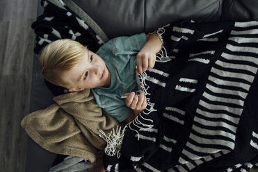 Blick von oben auf einen Jungen, der wegschaut, während er zu Hause auf dem Sofa liegt - CAVF59769