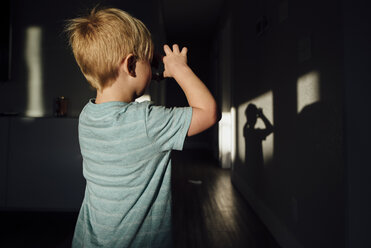 Rückansicht eines Jungen, der in der Dunkelkammer mit dem Sonnenlicht spielt - CAVF59770