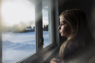 Seitenansicht eines nachdenklichen Mädchens, das zu Hause am Fenster steht - CAVF59779