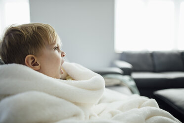 Seitenansicht eines Jungen, der gähnt, während er zu Hause auf dem Sofa sitzt - CAVF59783