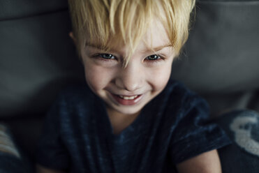 Hochformatiges Porträt eines lächelnden Jungen, der zu Hause auf dem Sofa sitzt - CAVF59786